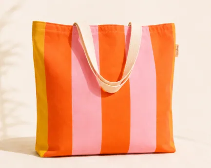Cabas en toile rayée orange et rose photographié sur fond sable